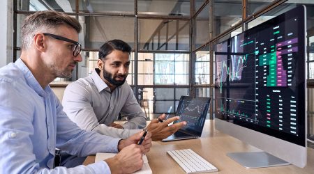 Two men analyzing financial data on computer screens