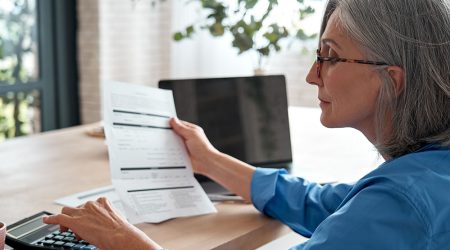 Senior woman examining financial papers with calculator